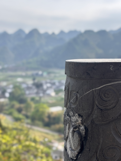 A carved stone pillar overlooking misty green mountains and a village