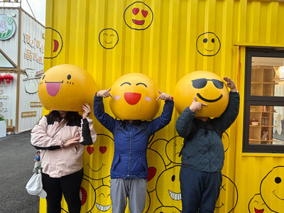 Three friends posing with smiley-face balloons in front of a yellow wall